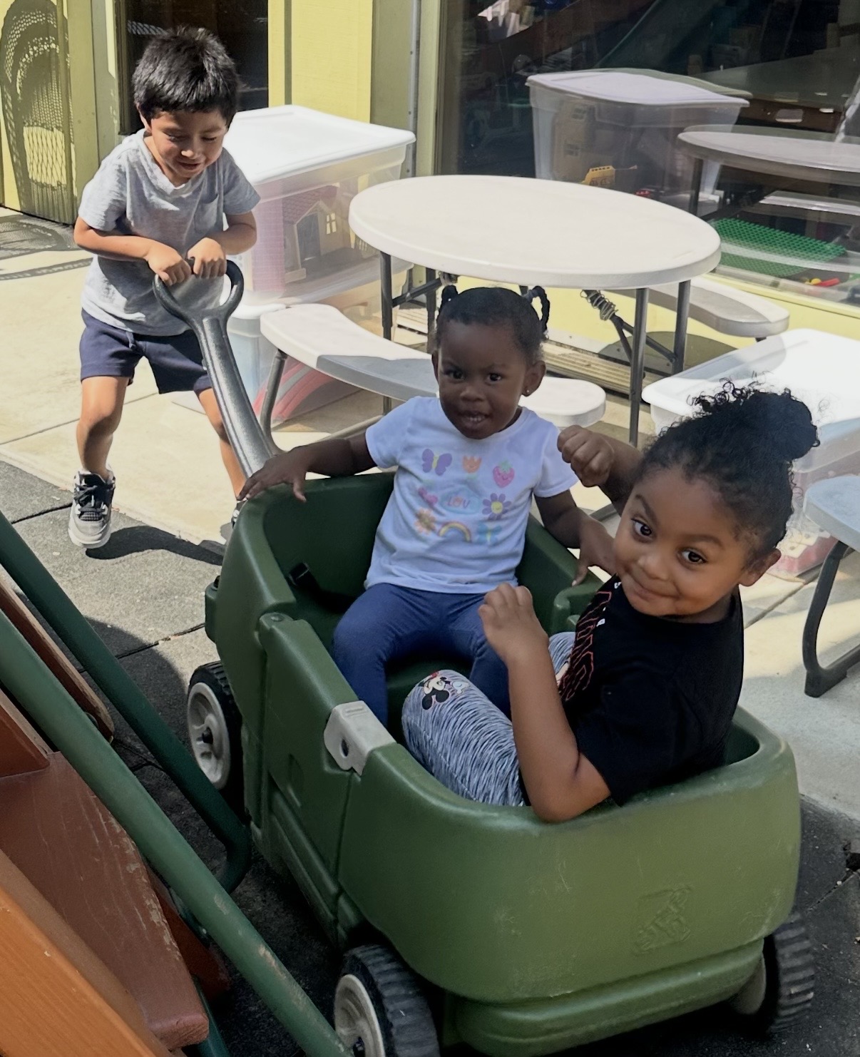Child pulling two friends in a green wagon