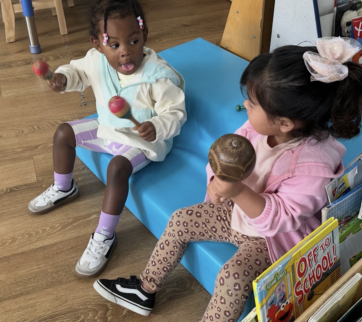 Two toddlers shaking maracas together on a play mat