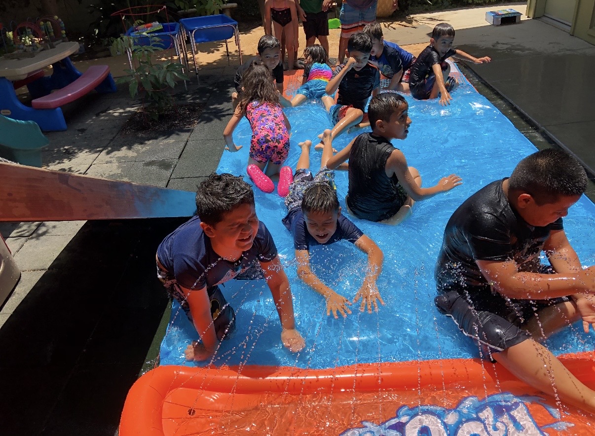 School-age children playing on a water slide in the yard on a hot day