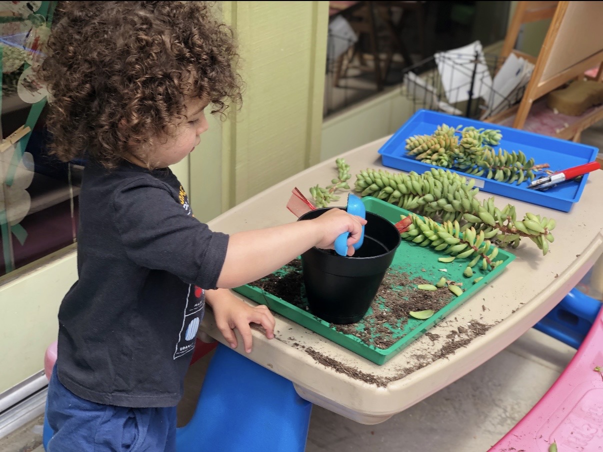 Toddler scooping soil into a pot at the potting table