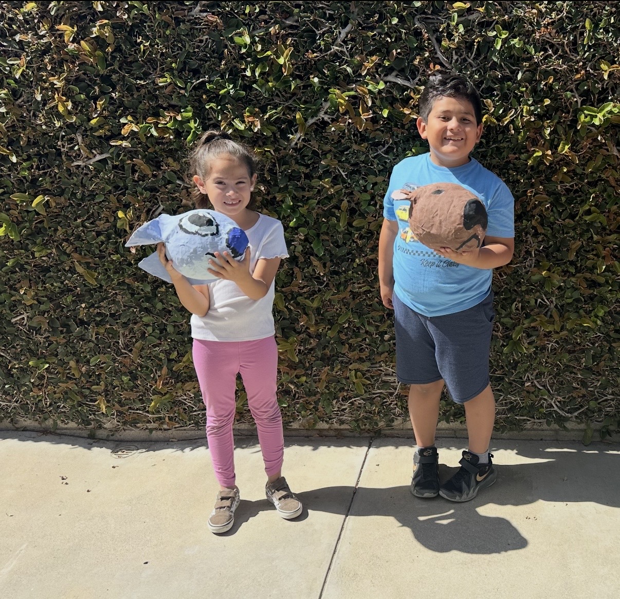 Two school-age children outside holding the papier-mâché animals they made