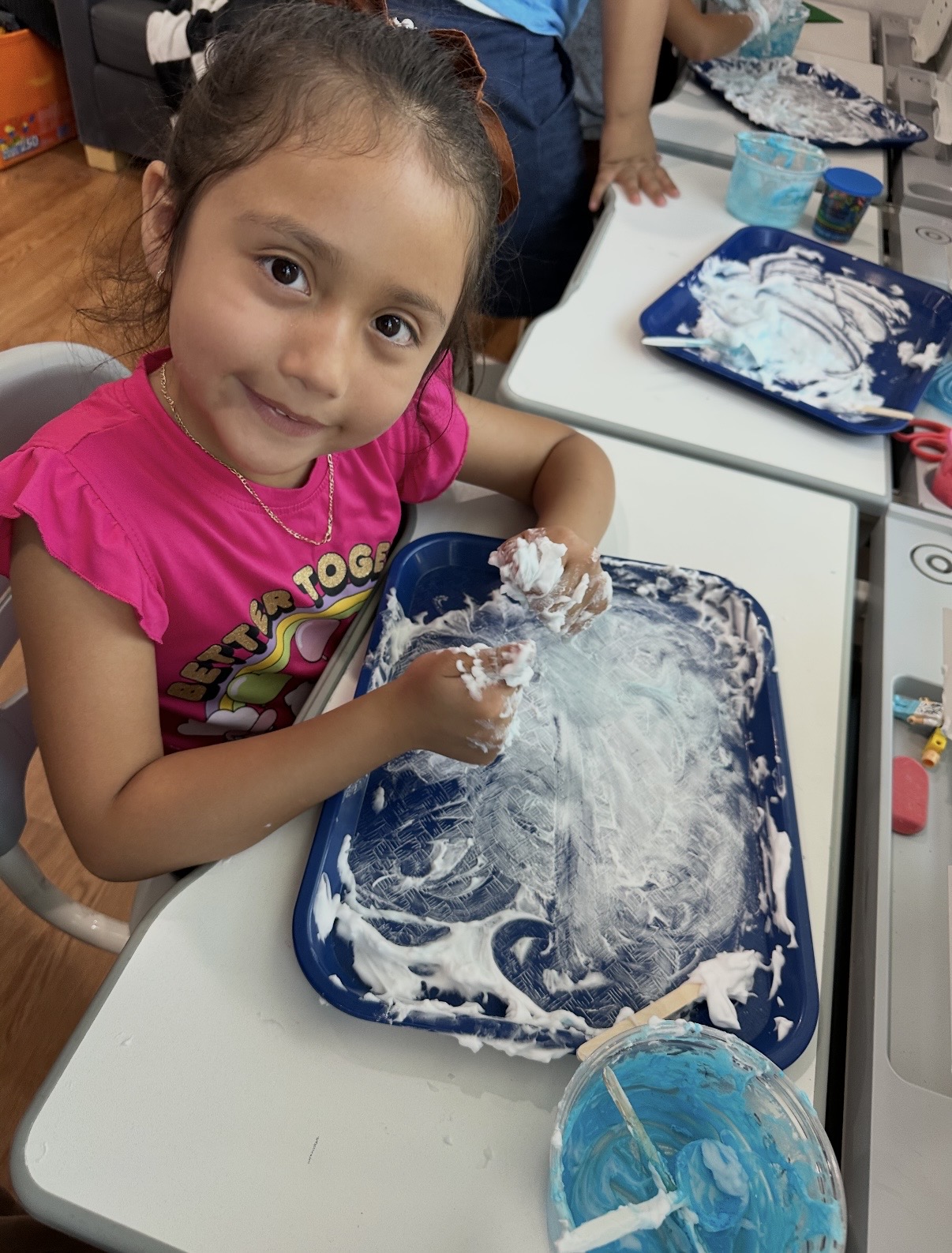 Child exploring shaving cream with both hands at the activity table