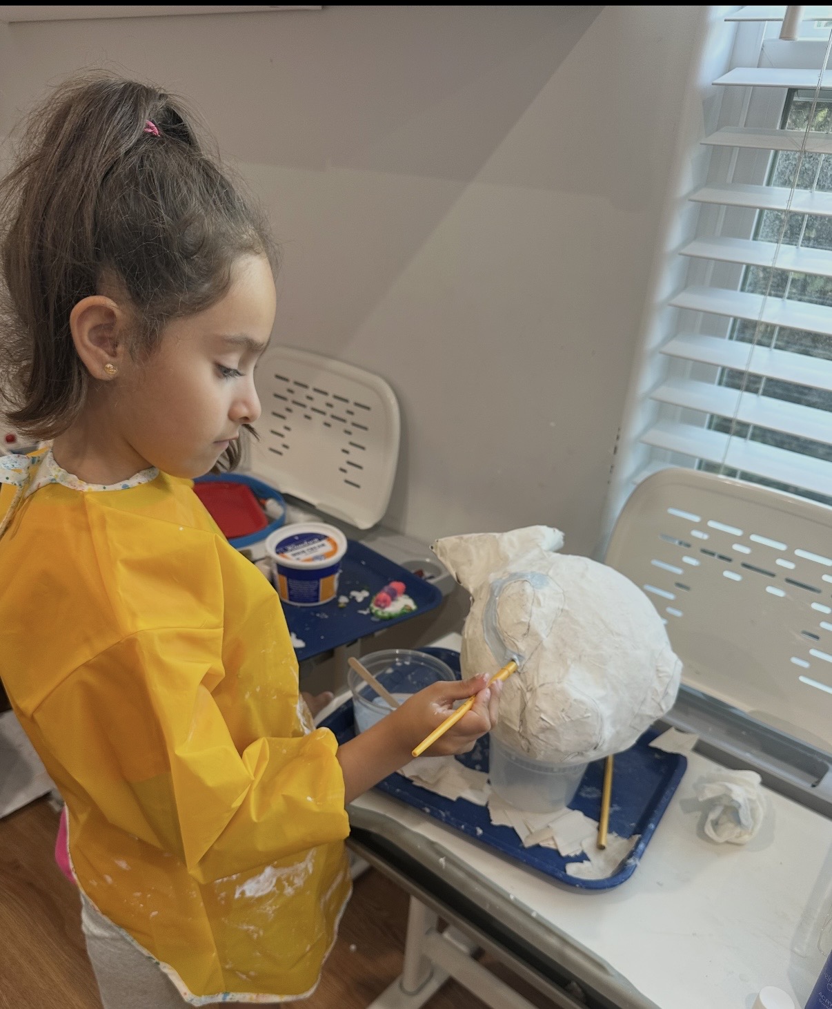 Child in a yellow smock painting a papier-mâché sculpture