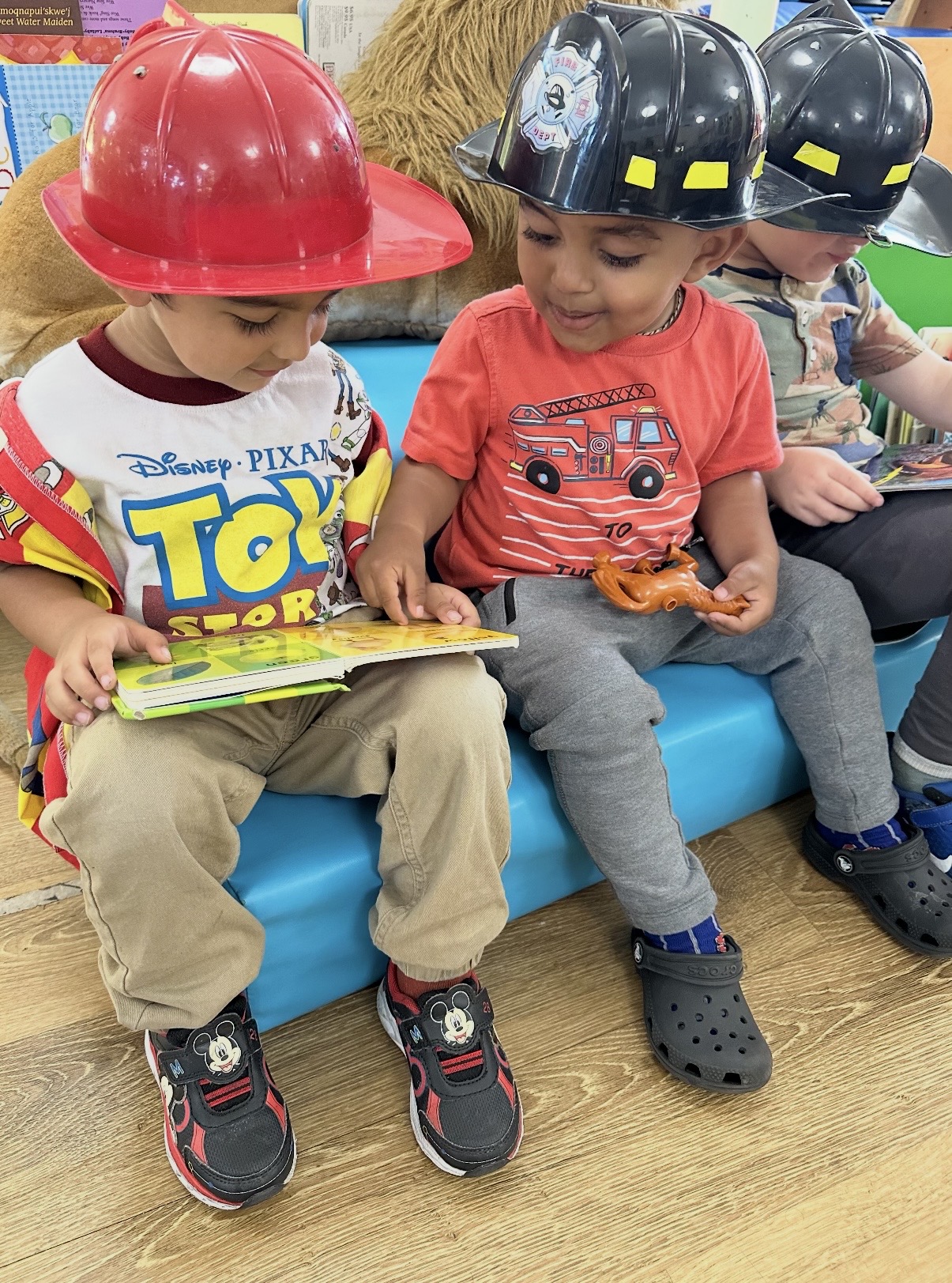 Two children in firefighter helmets reading a picture book together