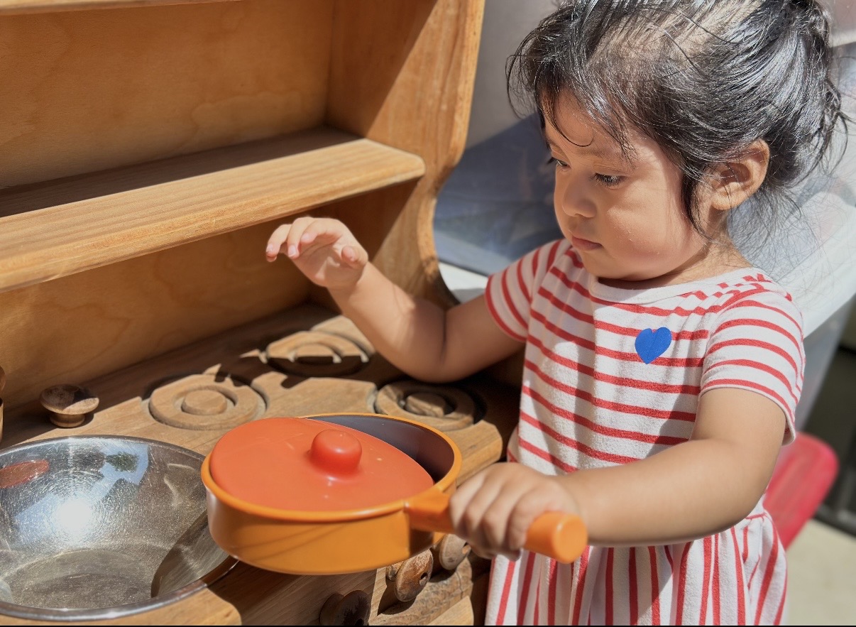 Toddler cooking at the wooden play kitchen